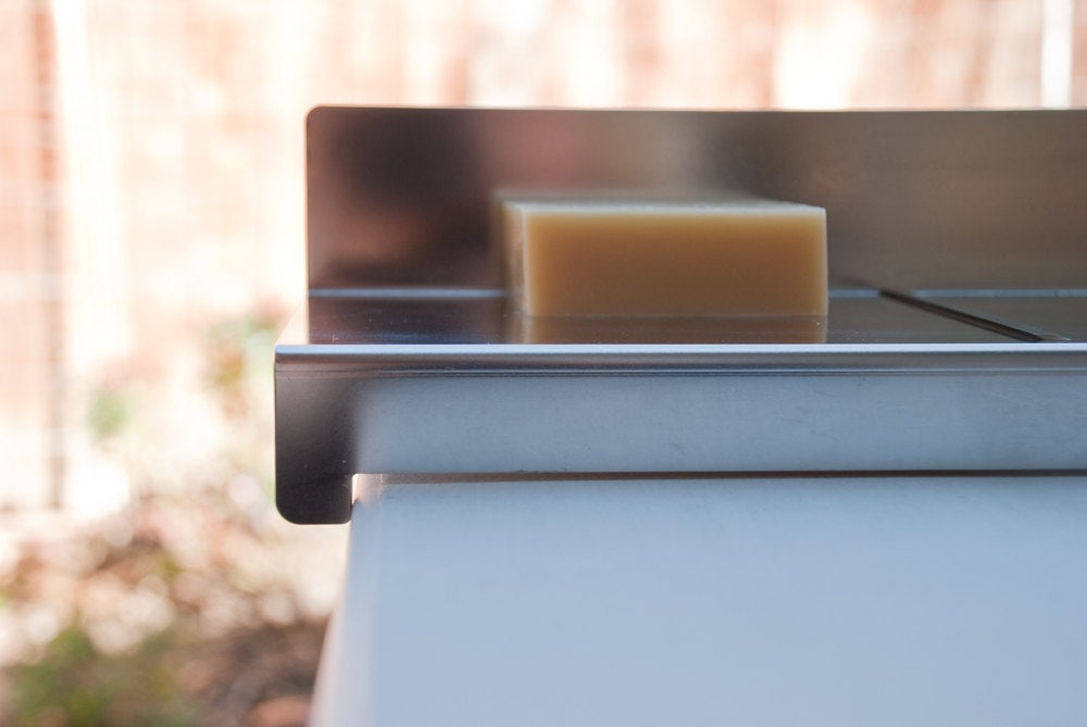 Heavy-duty bladeless stainless steel soap planer hooked on the edge of a table for effortless trimming.