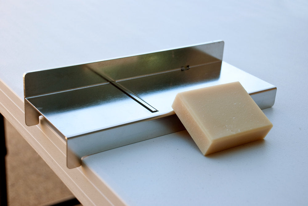 Heavy-duty bladeless stainless steel soap planer hooked on the edge of a table for effortless trimming.